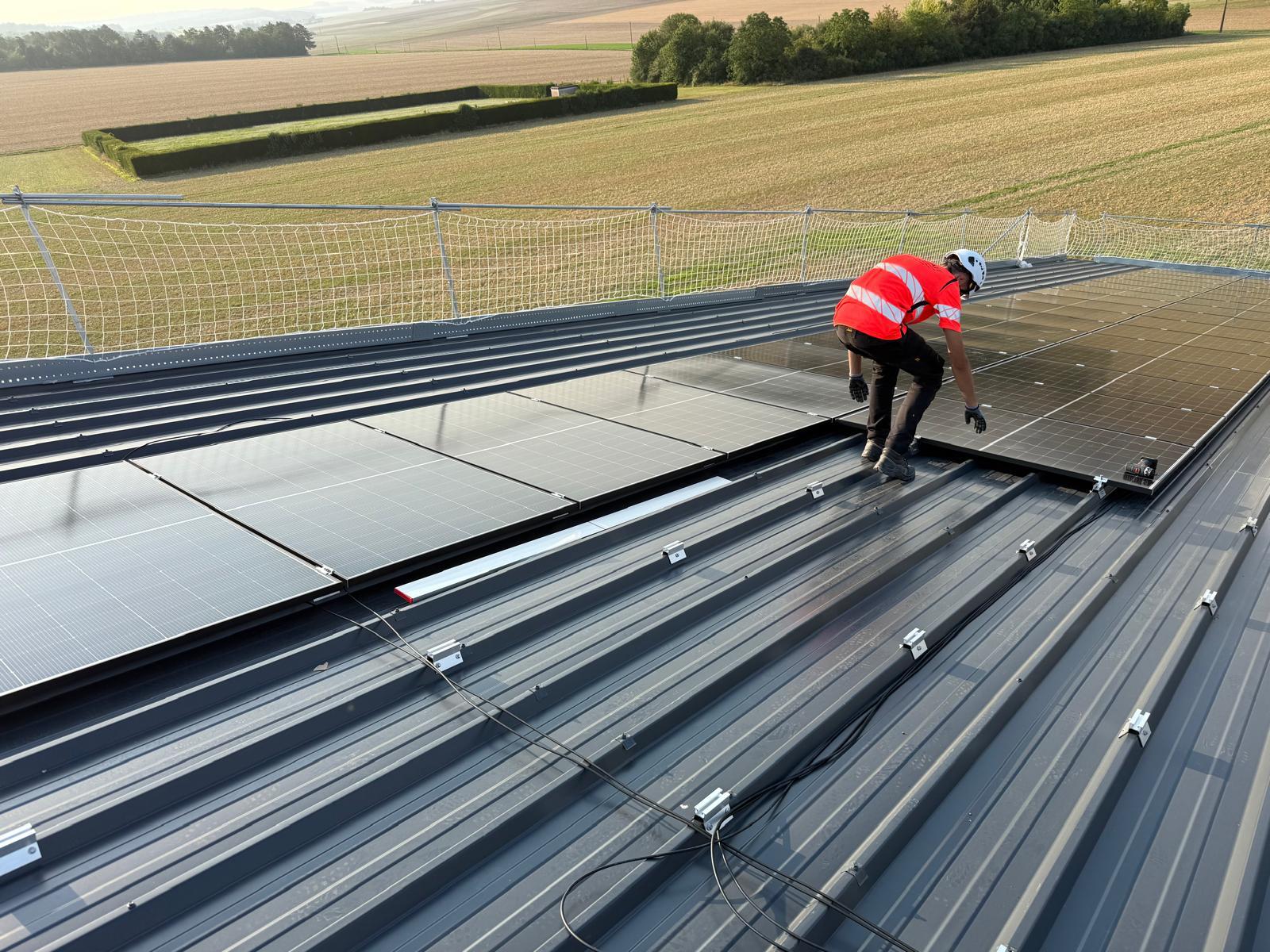 Technicien posant des panneaux solaires sur toiture inclinée, filet de sécurité en place